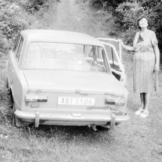 Woman standing beside vintage car on rural road.
