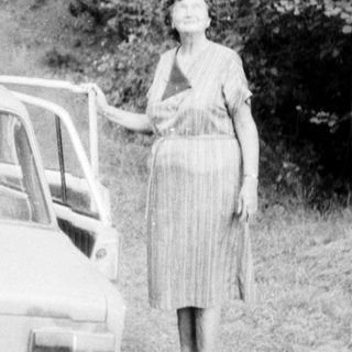 Woman standing beside vintage car on rural road.