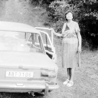 Woman standing beside vintage car on rural road.