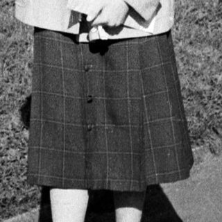 Woman in 1960s-style coat and skirt outdoors.