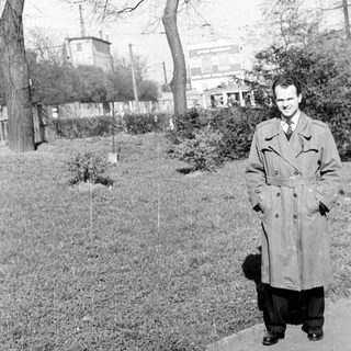 Man in 1950s-style coat walking outdoors in park.