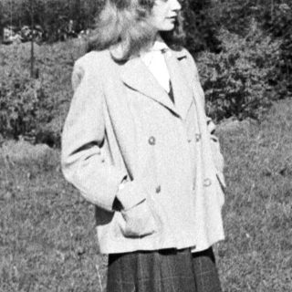 Woman in 1950s-style coat and skirt walking outdoors.