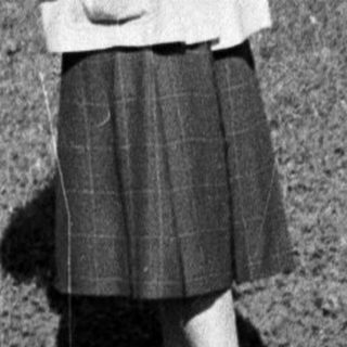 Woman in 1950s-style coat and skirt walking outdoors.
