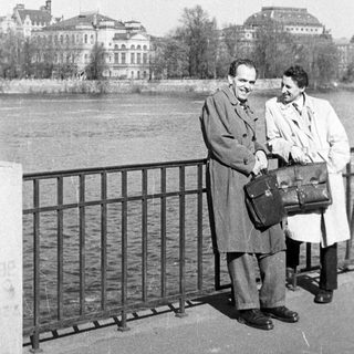 Two men posing by a river bridge.