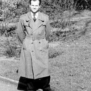 Man in vintage military-style coat on hillside road.