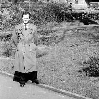 Man in vintage military-style coat on hillside road.