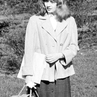 Young woman in 1960s-style coat and skirt carrying suitcase.