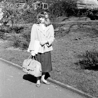 Young woman in 1960s-style coat and skirt carrying suitcase.