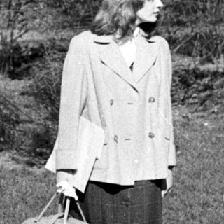 Woman walking with suitcase in park-like setting.
