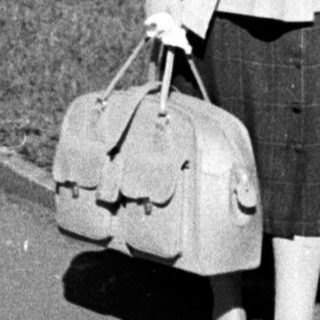 Woman walking with suitcase in park-like setting.
