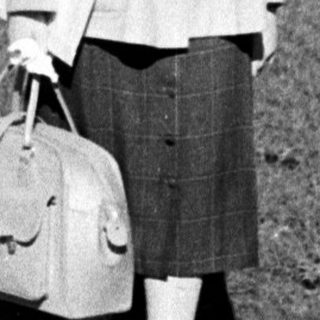 Woman walking with suitcase in park-like setting.