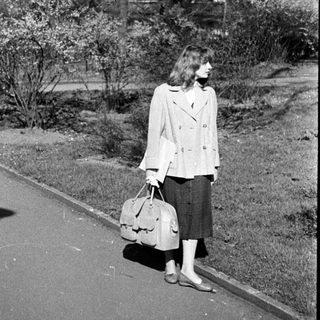 Woman walking with suitcase in park-like setting.