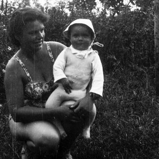 A woman holding a smiling infant outdoors.