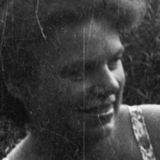 A woman holding a smiling infant outdoors.