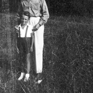 Two individuals standing outdoors in overgrown grass.