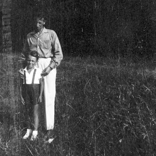 Two individuals standing outdoors in overgrown grass.