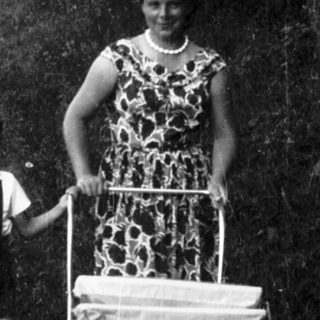 A woman pushing a cart with a child beside her outdoors.