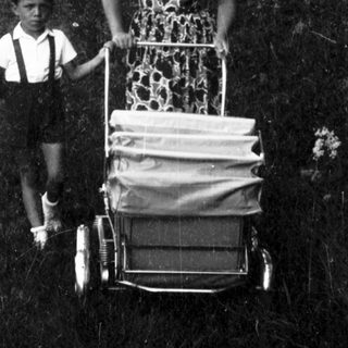 A woman pushing a cart with a child beside her outdoors.