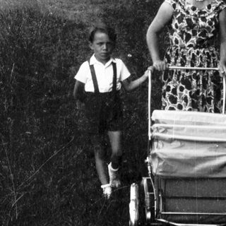 A woman pushing a cart with a child beside her outdoors.