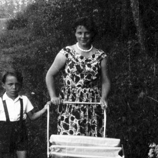 A woman pushing a cart with a child beside her outdoors.