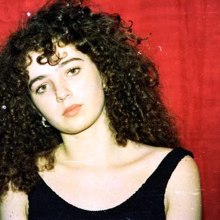 Curly-haired woman in black top against red background.