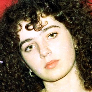 Curly-haired woman in black top against red background.