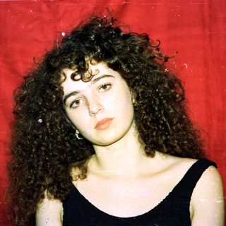 Curly-haired woman in black top against red background.