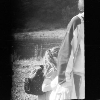 Two people standing near water, one holding a bag.