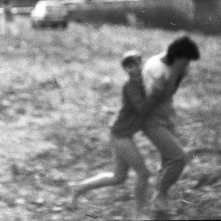 Two individuals running through a muddy, rural area.