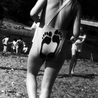 People at outdoor gathering near waterfront, wearing 1970s-style swimwear.