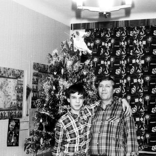 Two men posing indoors near decorated Christmas tree.