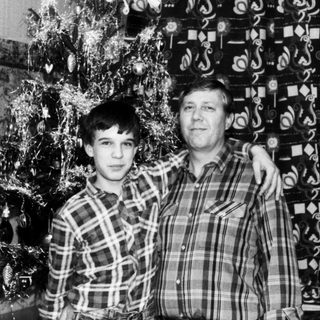 Two men posing indoors near decorated Christmas tree.