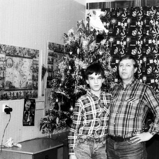 Two men posing indoors near Christmas tree.