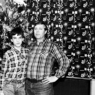 Two men posing indoors near Christmas tree.
