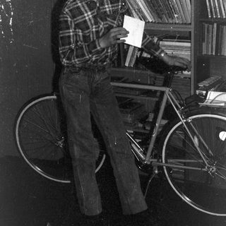 Young person holding envelope near bicycle in cluttered room.