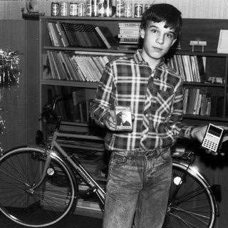 Young boy holding calculator beside bicycle in book-filled room.
