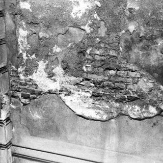 Damaged wall with exposed brick and plaster cracks.