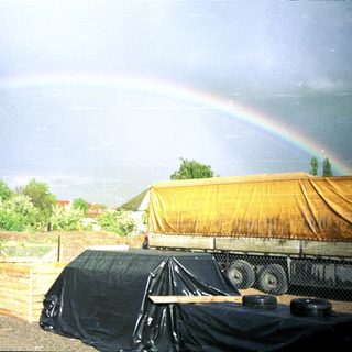 Rainbow over construction site with covered trucks.