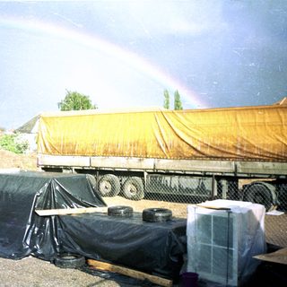 Construction site with truck, tarps, and rainbows after rain.
