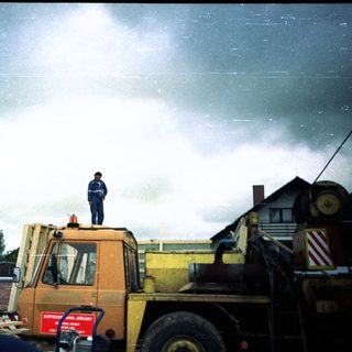 Construction worker standing on heavy machinery in rainy weather.