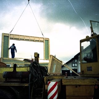 Construction worker installing large window frame with crane.