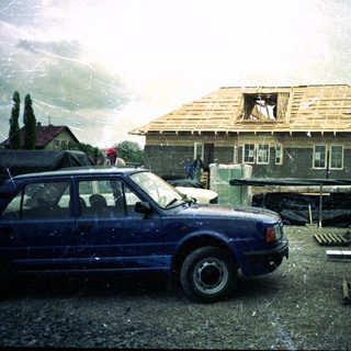 House under construction or repair, rain, blue car parked.