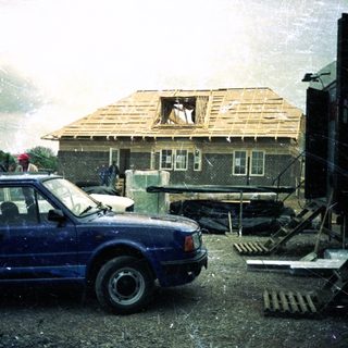 House under construction or repair, rain, blue car parked.