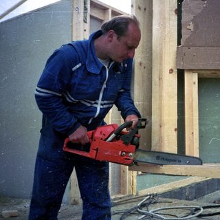 Man using chainsaw on wooden structure.