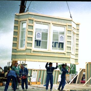 Construction workers lifting prefabricated house section.