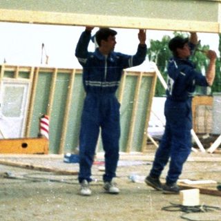 Construction workers lifting prefabricated house section.