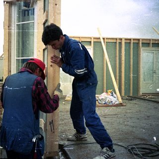 Two workers assembling wooden frame structure outdoors.