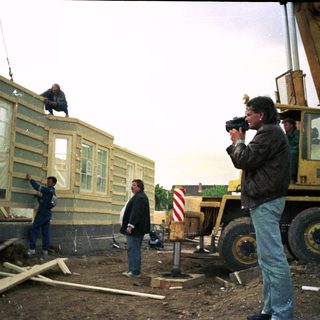 Construction site with modular home being lifted by crane.