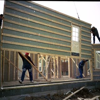 Construction workers installing exterior siding on a house frame.