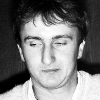 Young man indoors, wearing sweater, looking downward.
